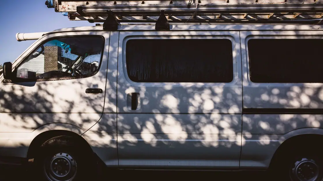 Side of a plain white work van with a ladder rack