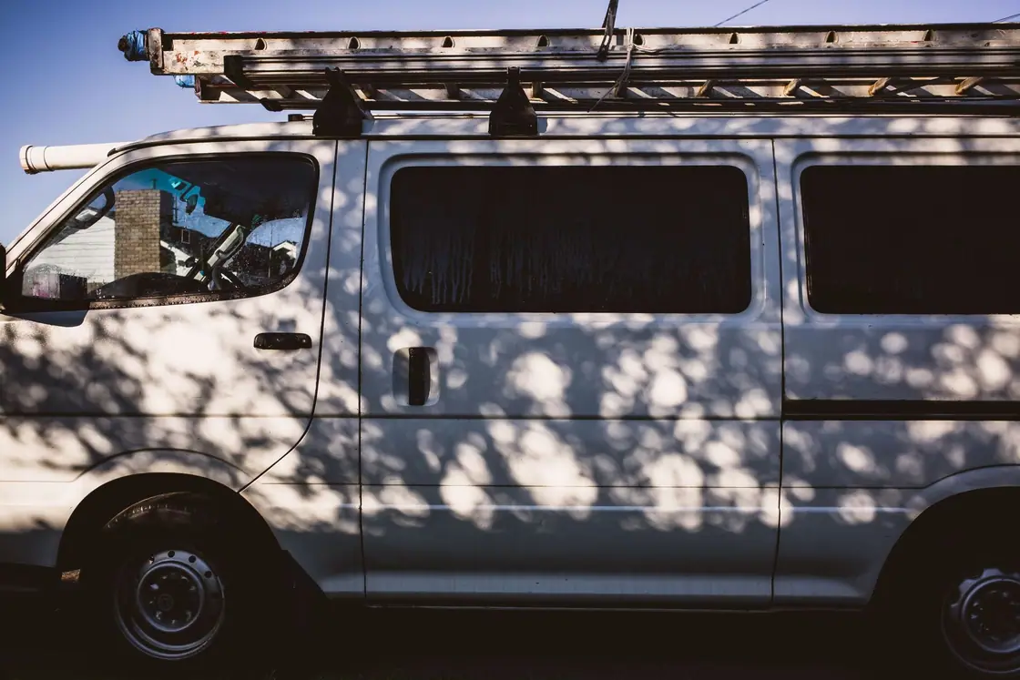 Side of a plain white work van with a ladder rack