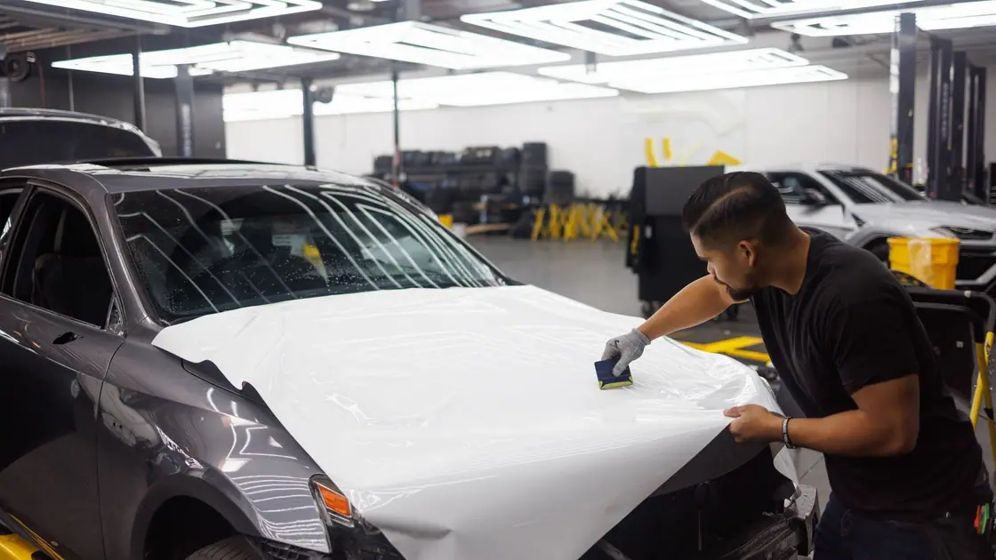 Installer squeegeeing white wrap vinyl across a car hood in a workshop