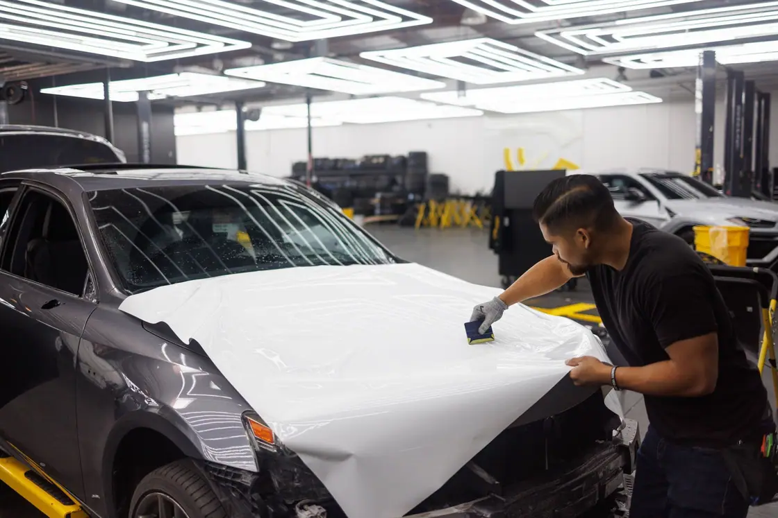 Installer squeegeeing white wrap vinyl across a car hood in a workshop